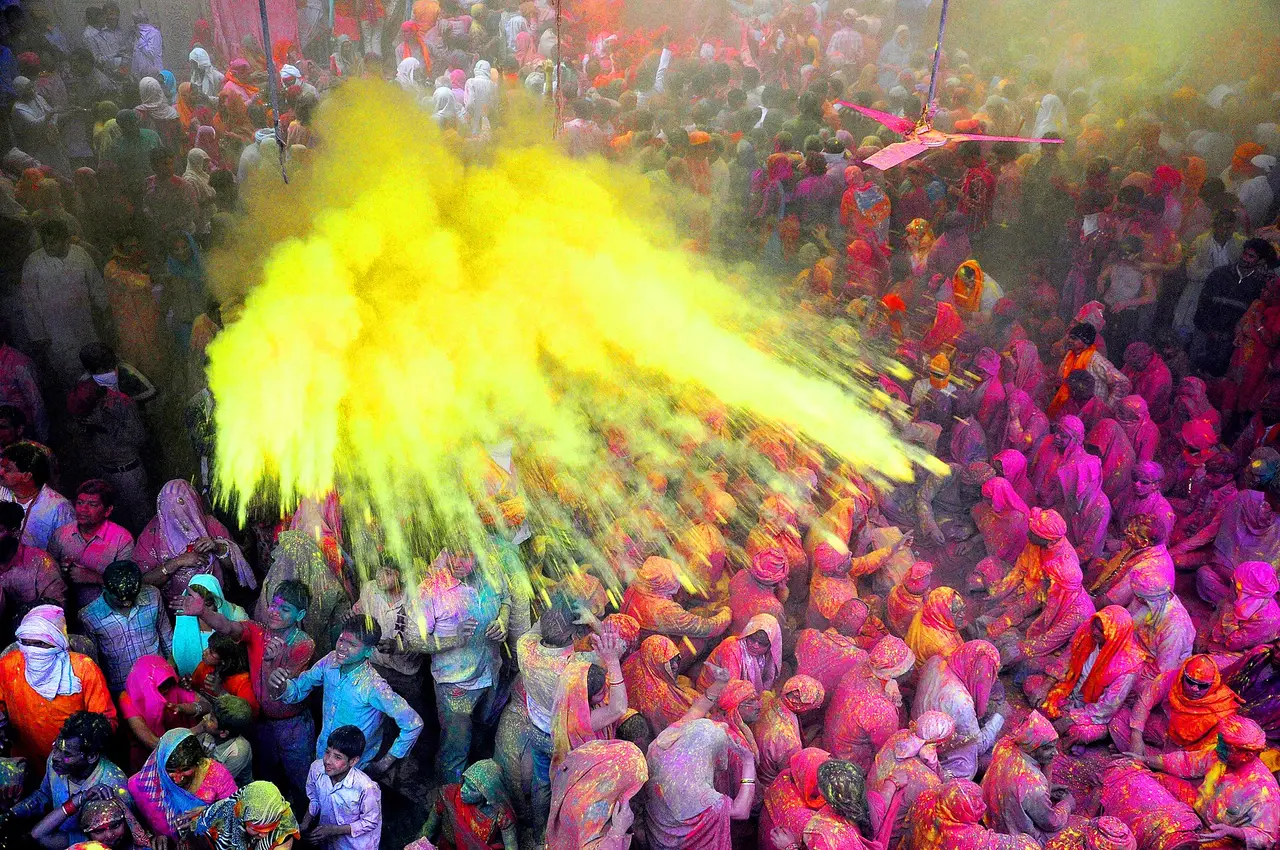 A crowd covered in colour as yellow powder bursts overhead