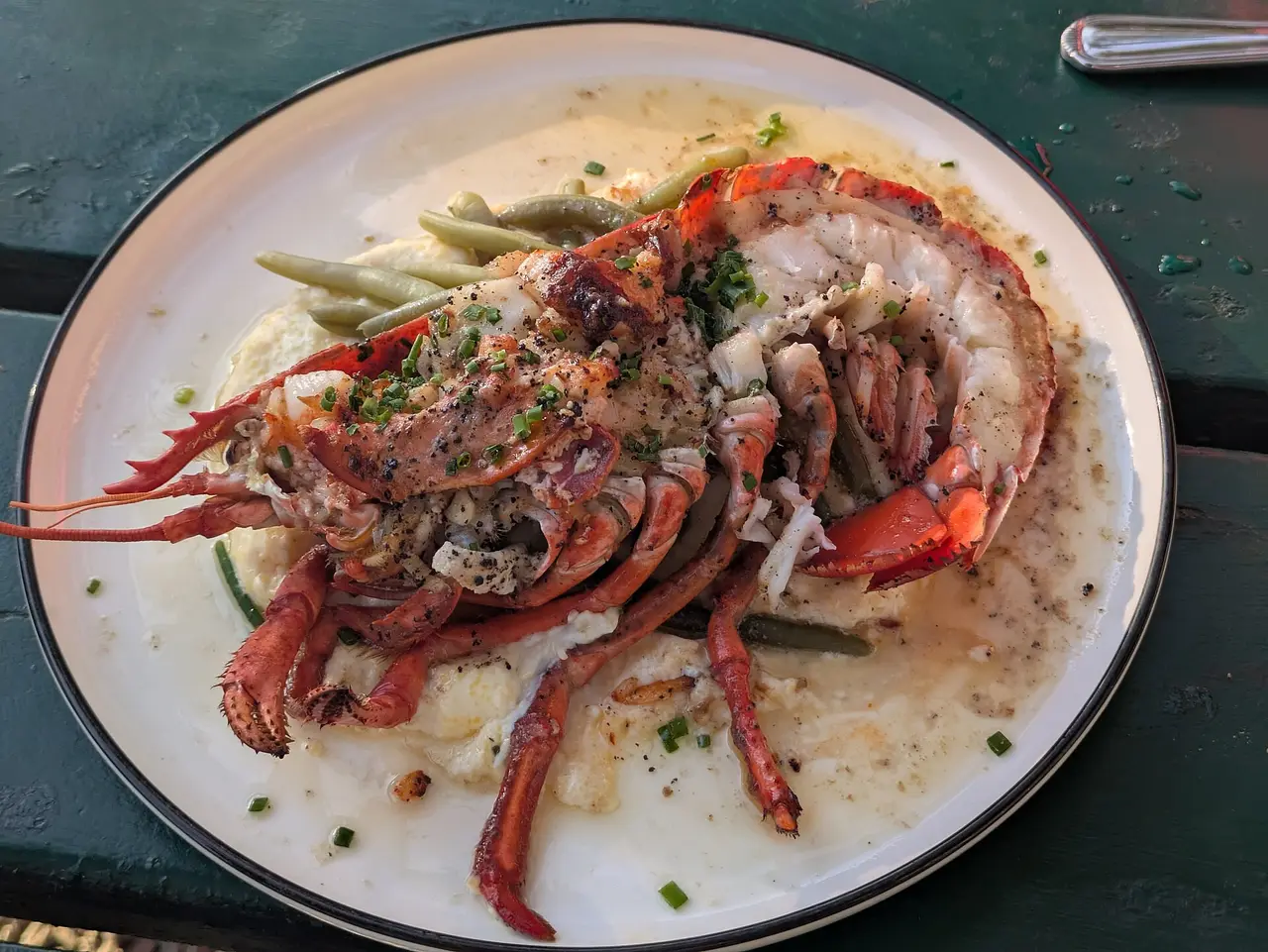 A halved lobster served on a white plate with green beans