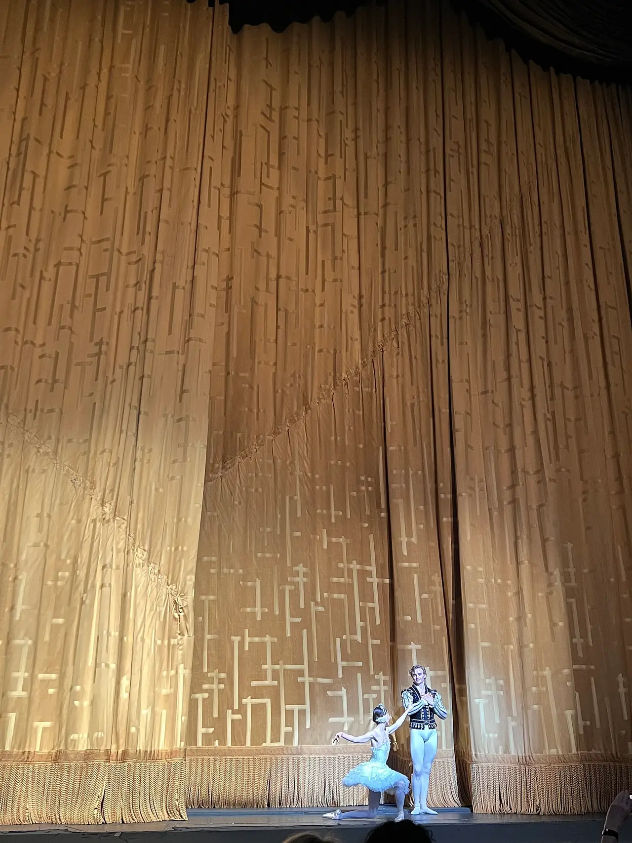 Two small dancers on stage in front of a tall gold curtain