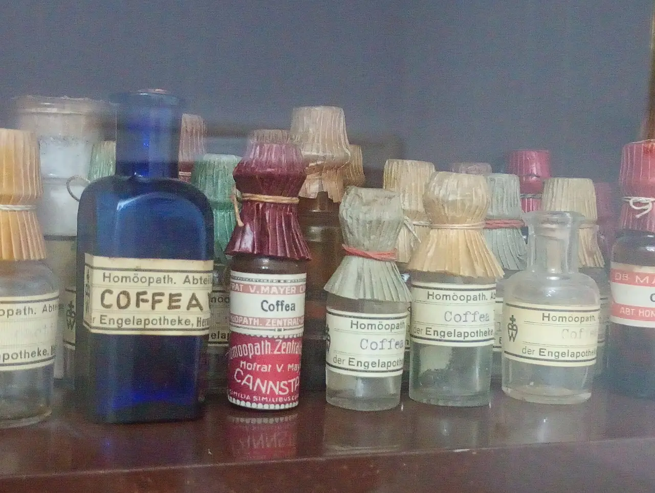 Rows of small old glass bottles with paper labels on a shelf