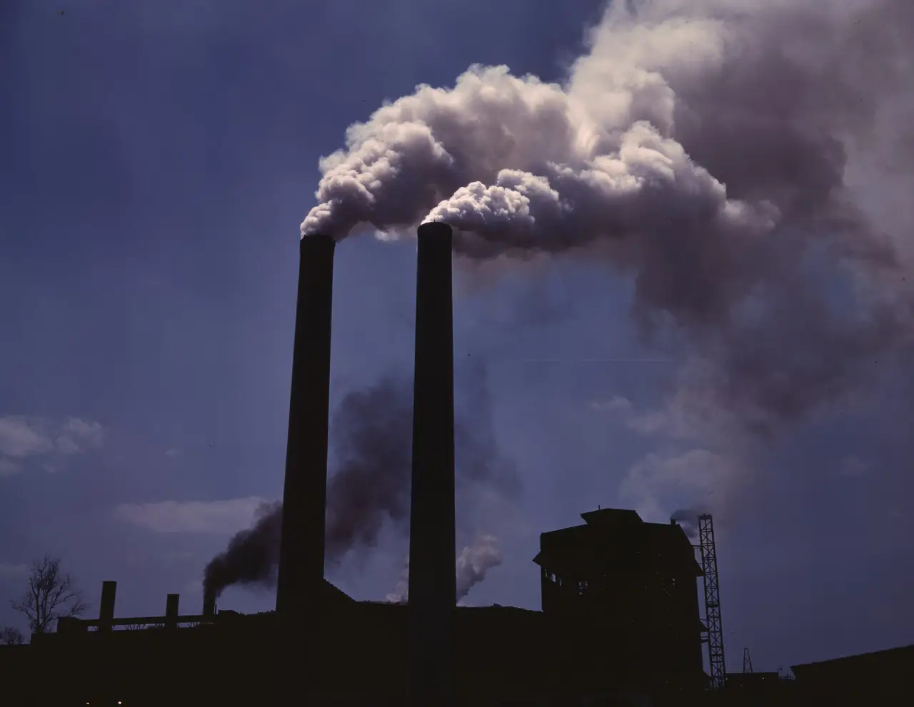 Two tall smokestacks releasing thick smoke against a blue sky
