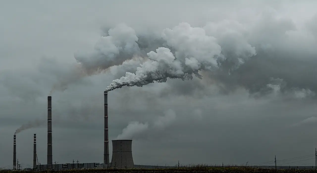 Grey smoke rising from tall factory chimneys under an overcast sky