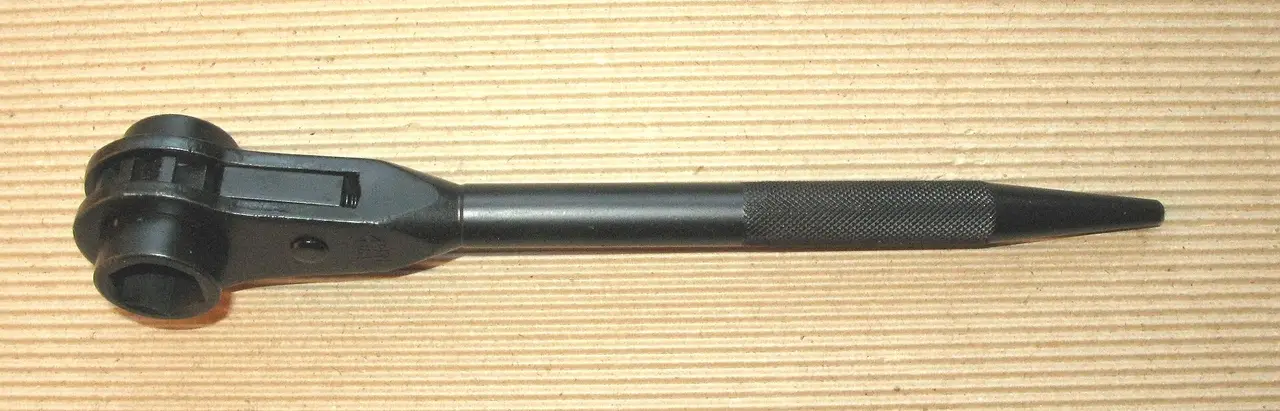 A steel ratchet wrench lying on a pale wooden surface