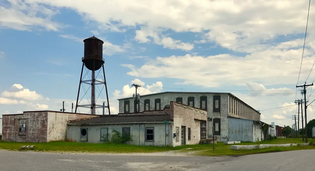 A disused factory building with a water tower beside a road