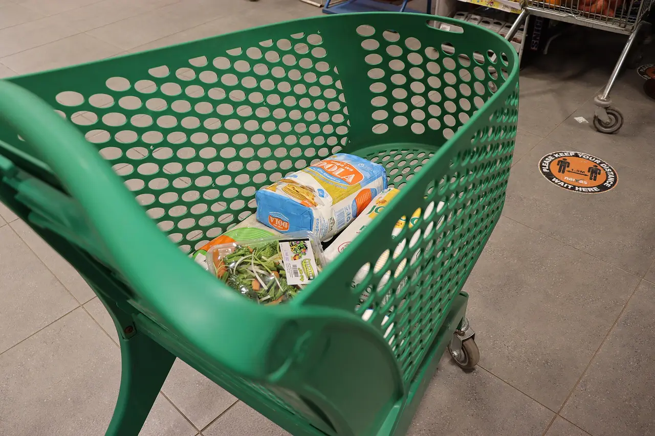 A green plastic shopping cart with a few items on a supermarket floor