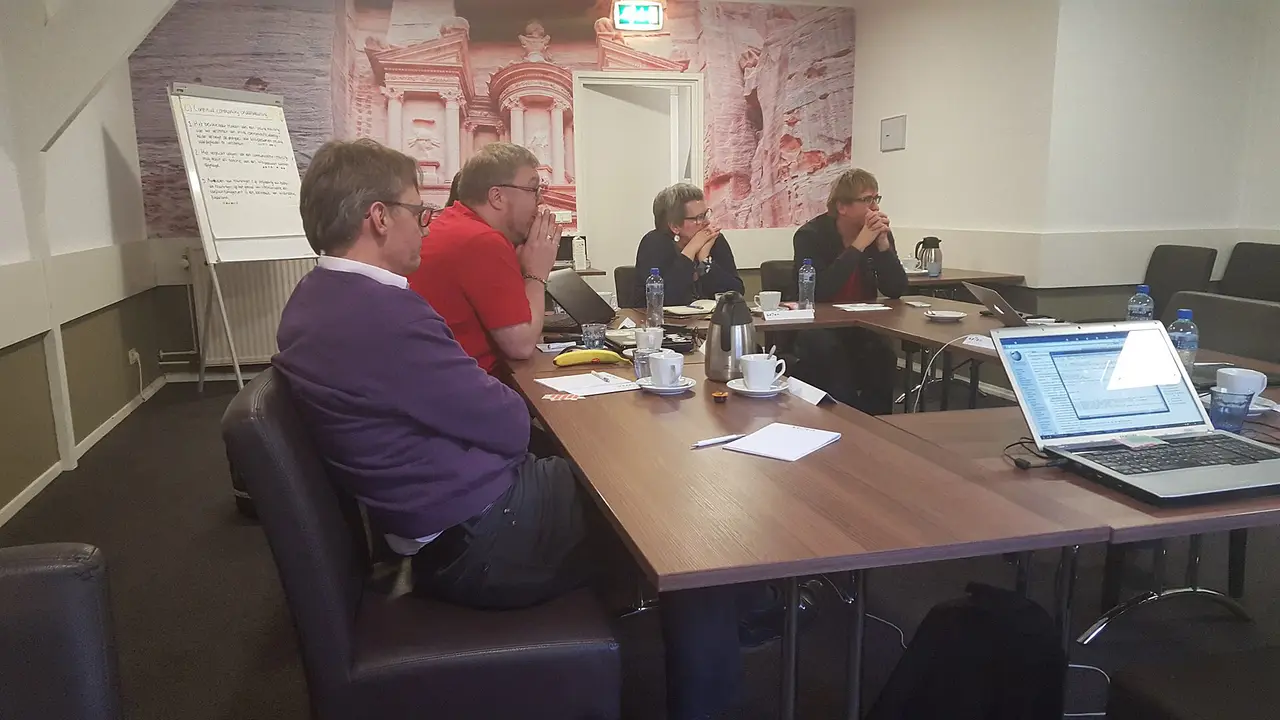 Colleagues seated around a meeting room table with laptops