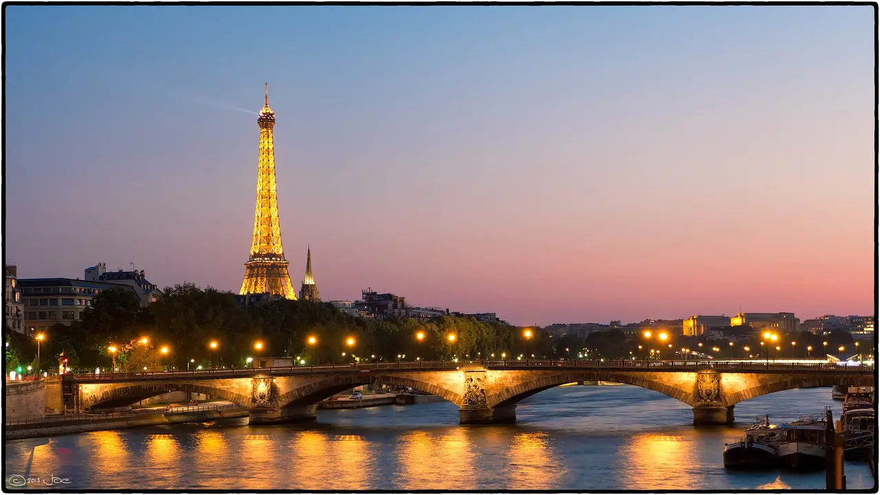 The lit Eiffel Tower beyond a bridge over the Seine at dusk