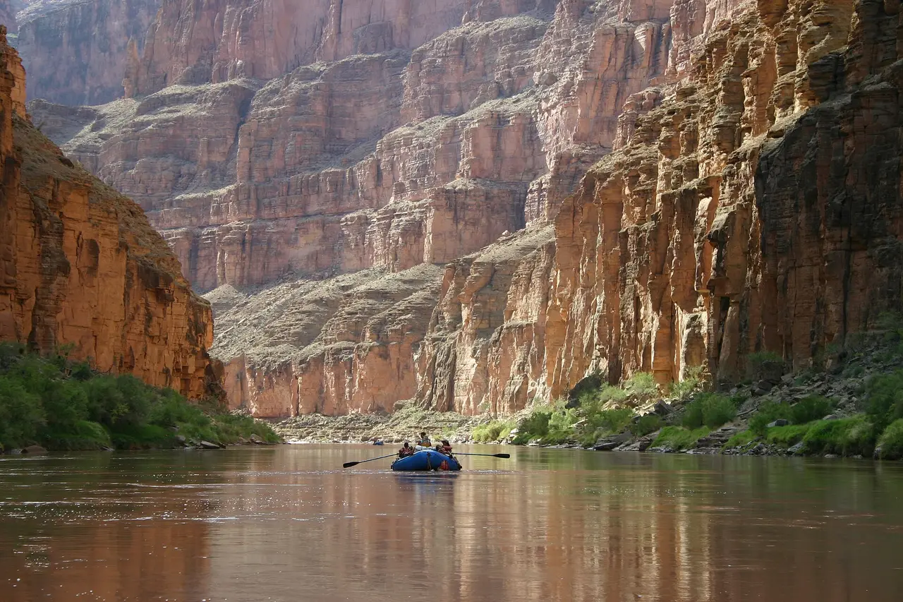 A small raft on a calm river between tall red canyon cliffs