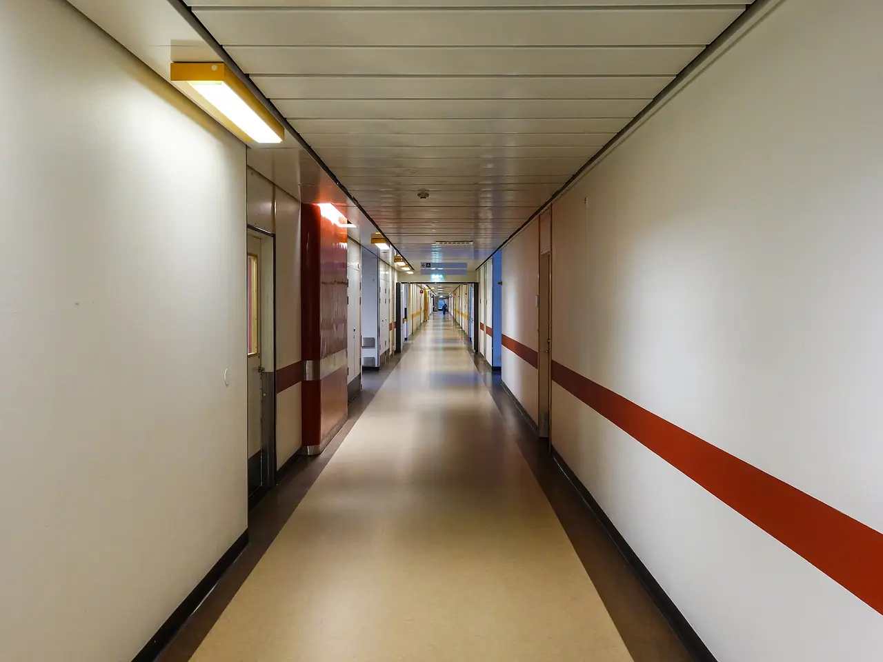 A long empty hospital corridor with white walls and a red stripe