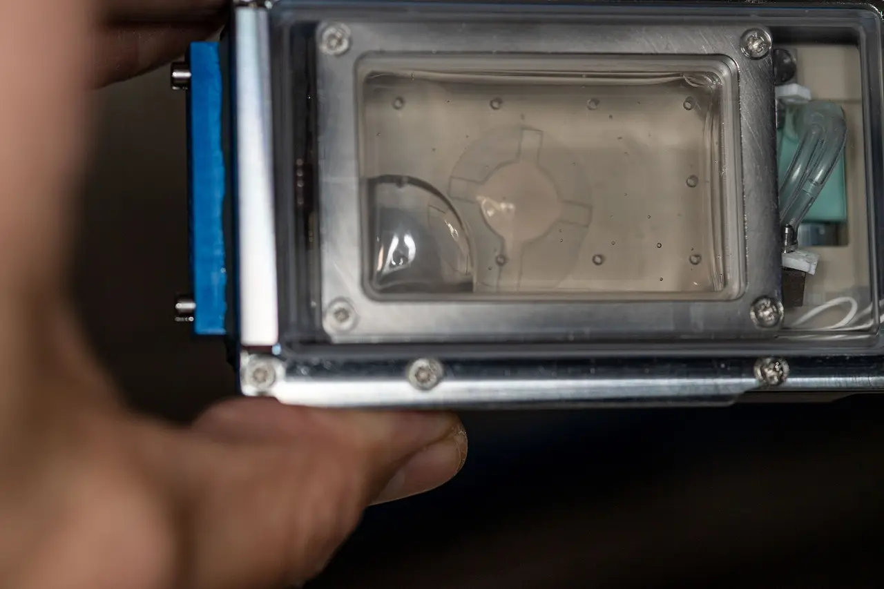 A hand holding a clear-windowed experiment container