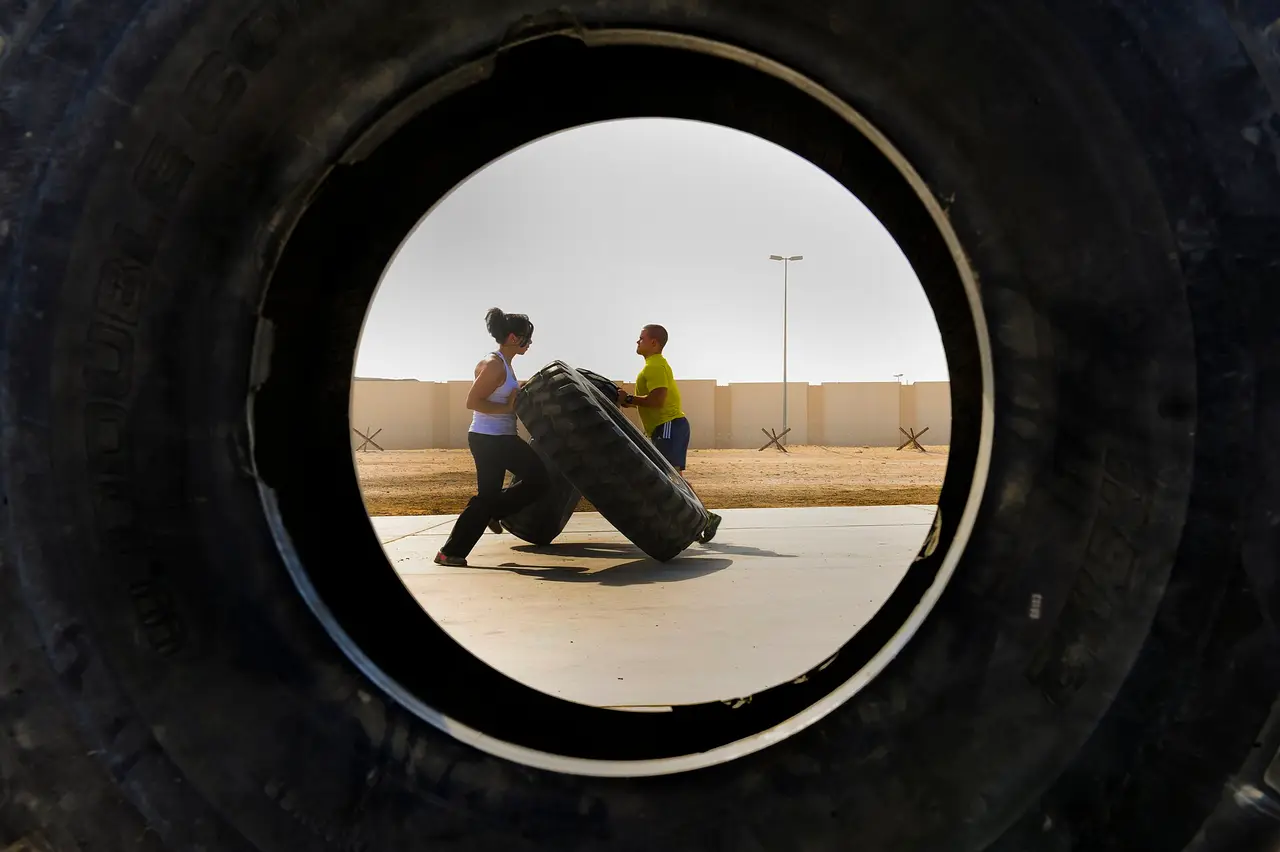 A large black tyre framing two distant people flipping another tyre