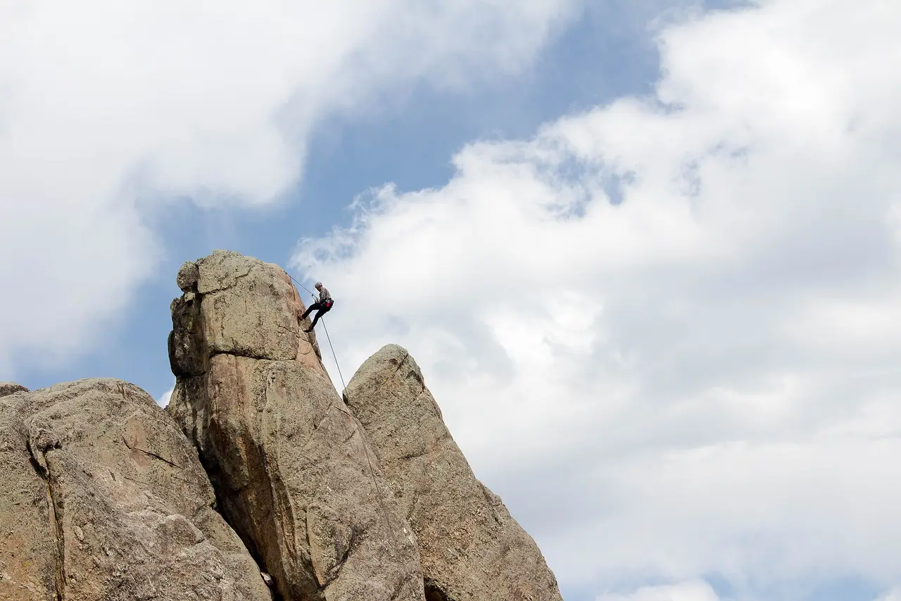 A climber on a rope at the top of a granite rock tower