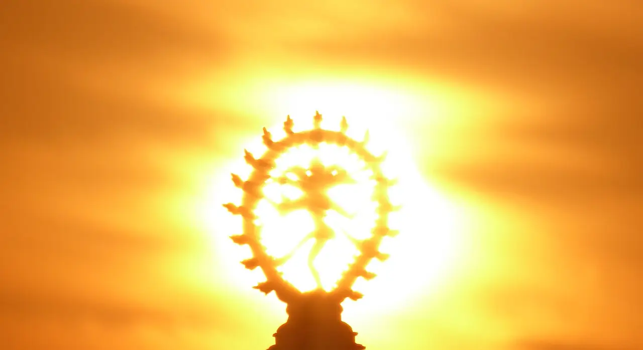 Silhouette of a dancing Shiva figurine within a ring, in front of the sun