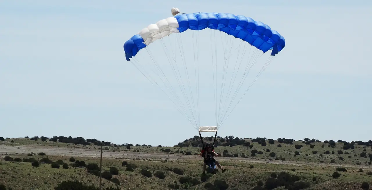 A parachutist with a blue and white canopy landing in open country
