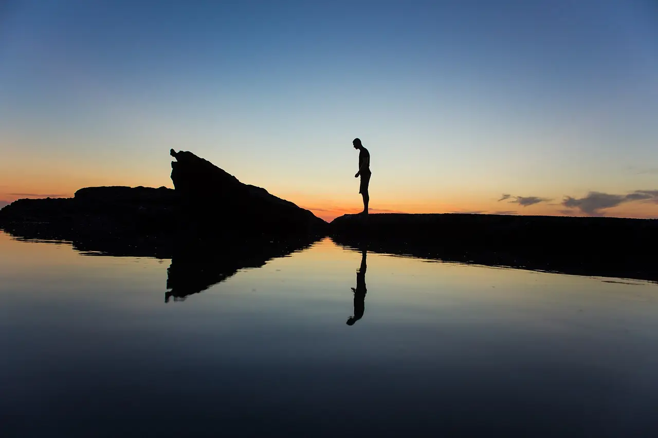 A man's dark silhouette on a shore against a sunset sky