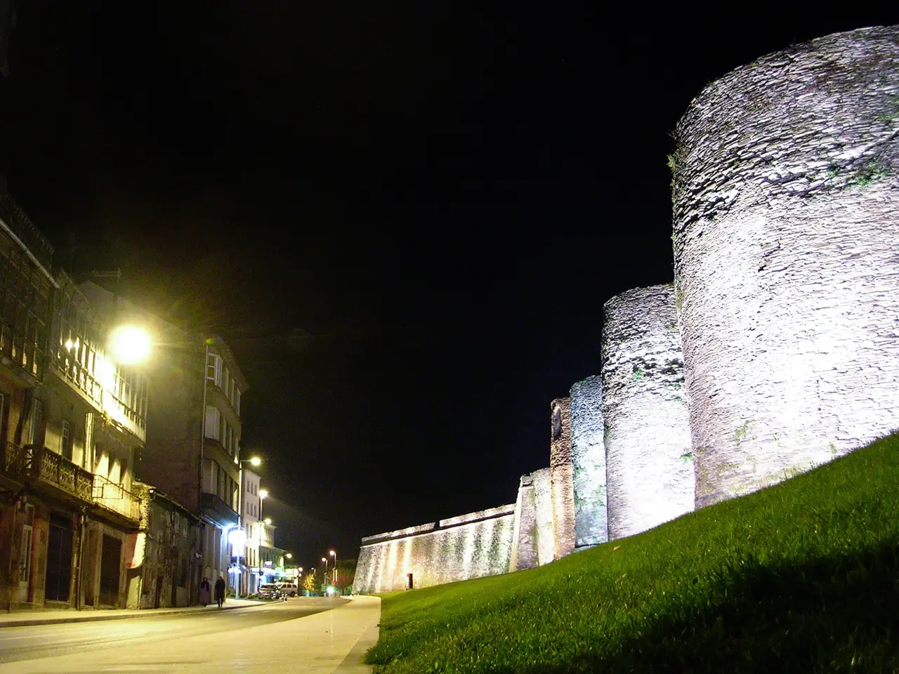 Floodlit Roman wall with round towers beside a night-time street
