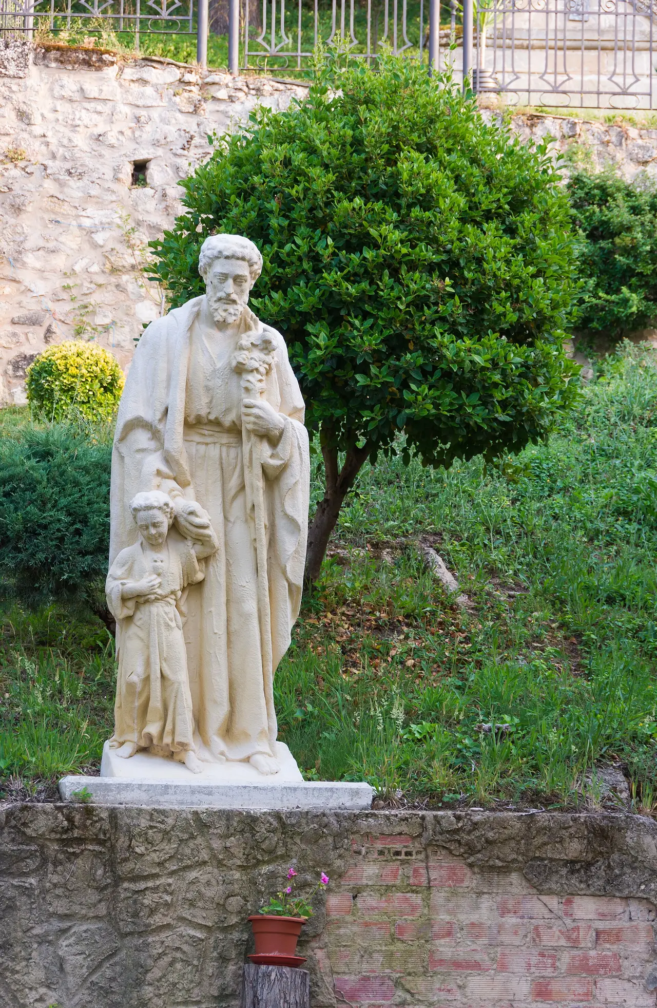 White statue of Saint Joseph carrying the child Jesus in a garden