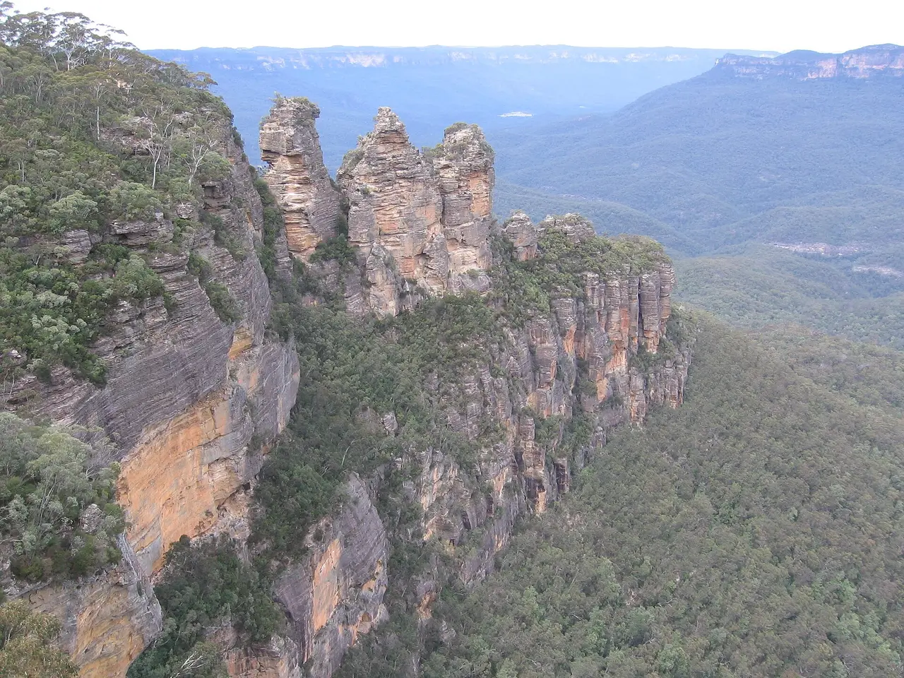 Three rock pillars beside a cliff above a forested valley