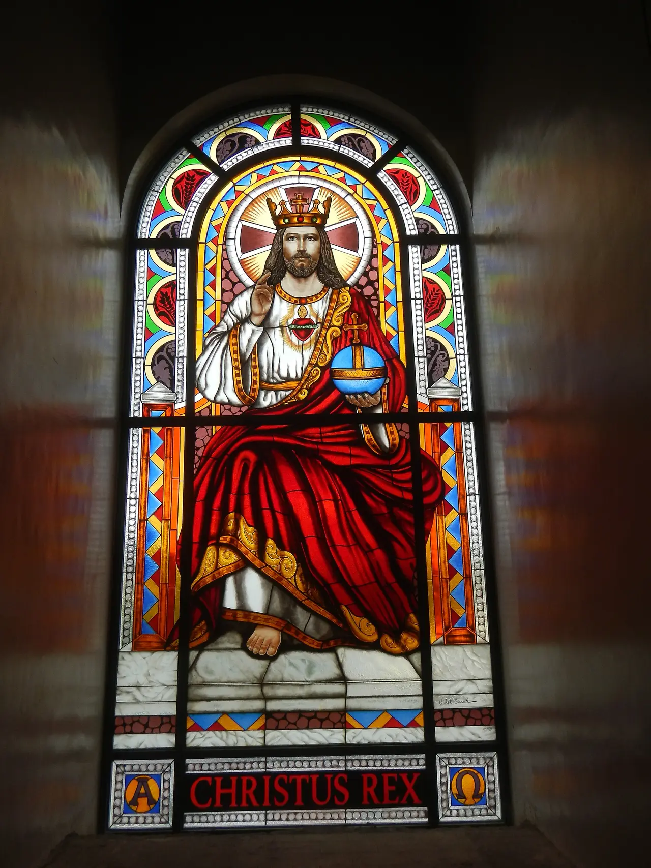 A stained glass window of a crowned Christ in red robes