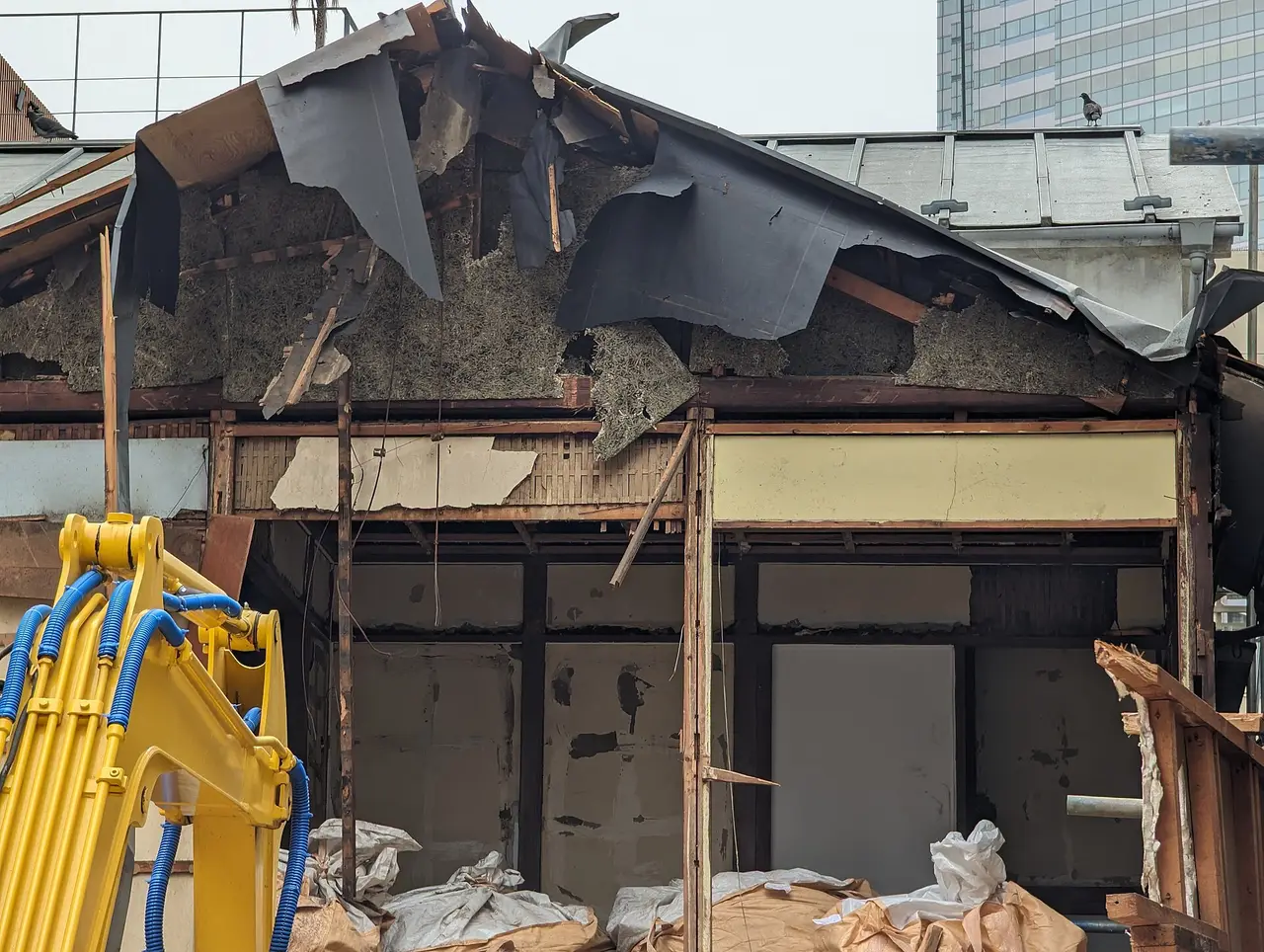 A partly demolished house with exposed floors and a yellow excavator arm