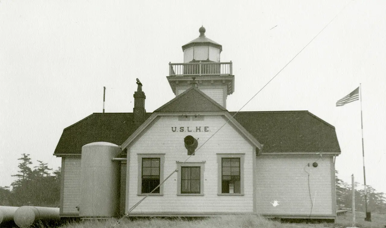 A small white lighthouse with a square tower and a flag