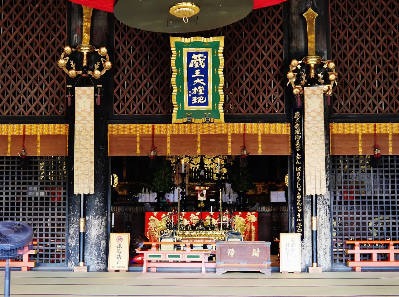 A temple hall with wooden pillars, a gold altar and tatami floor