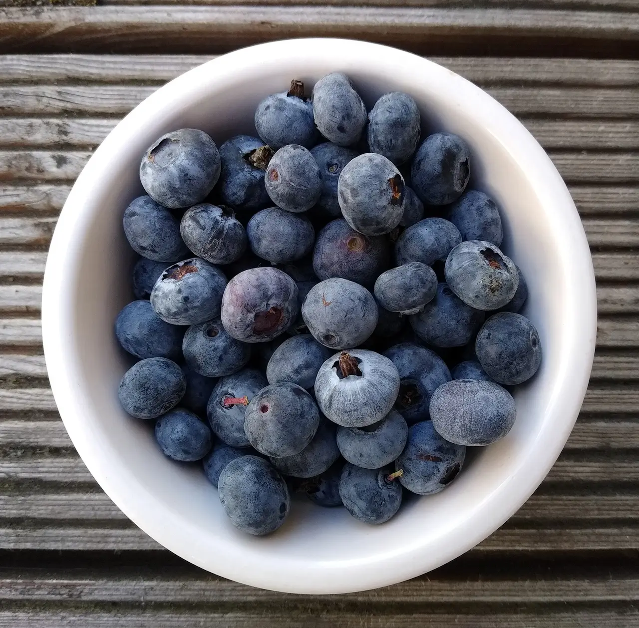 A white bowl of blueberries seen from above on a wooden table