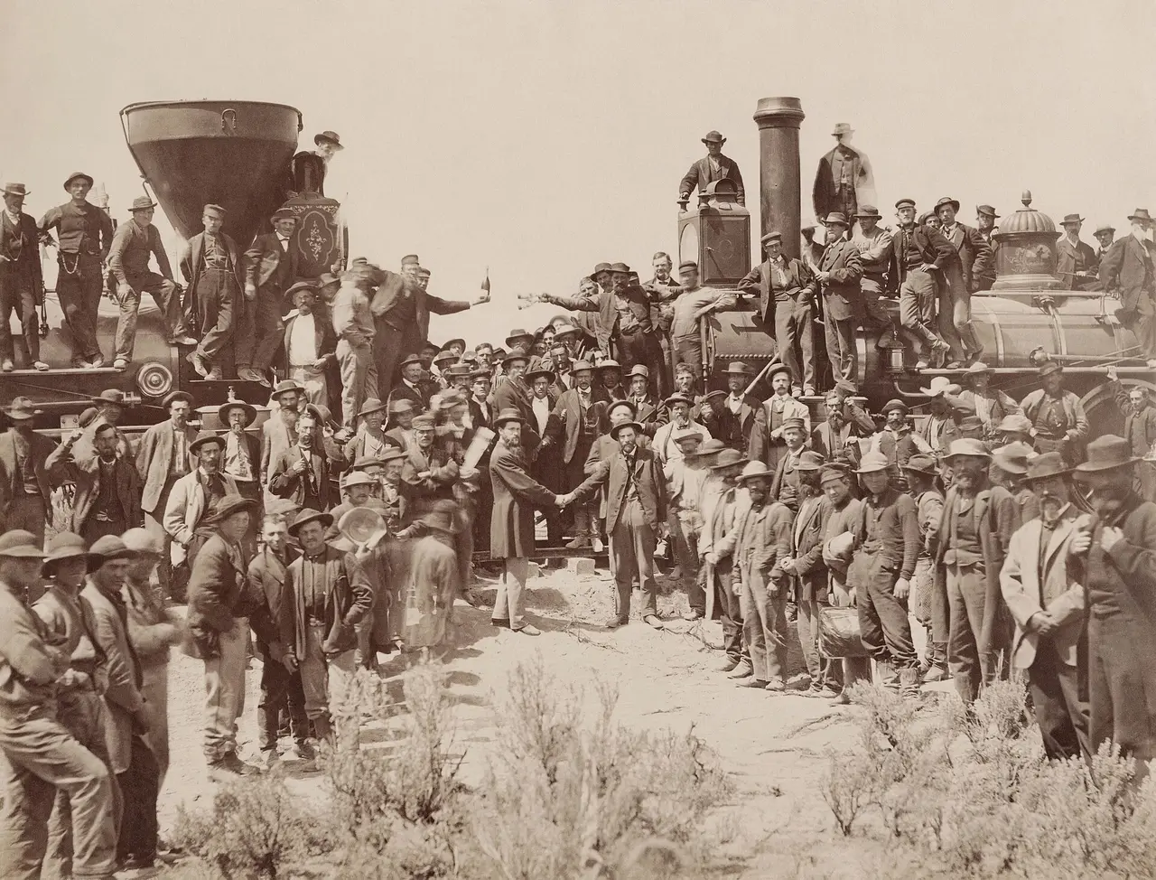 Crowd of railway workers around two locomotives, two men shaking hands