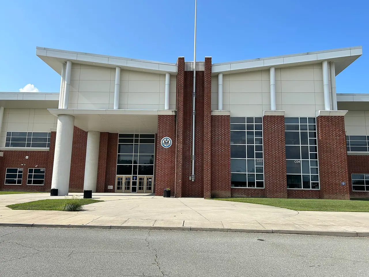 Brick school entrance with white columns and a flagpole against a blue sky