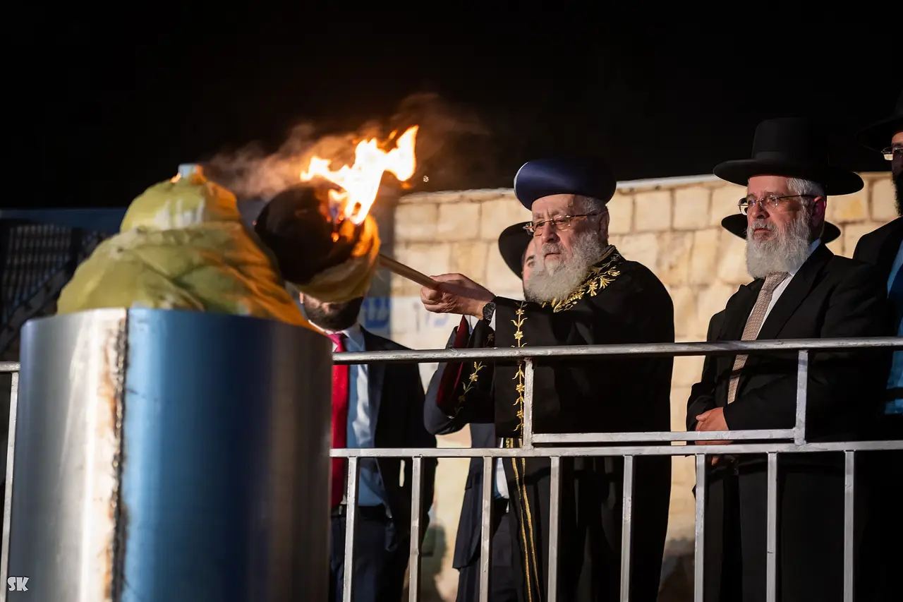 A rabbi holds a torch to a bonfire at night as men watch