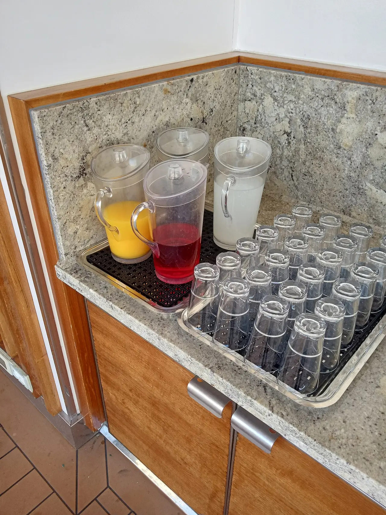 Jugs of coloured drinks on a granite counter next to a tray of cups