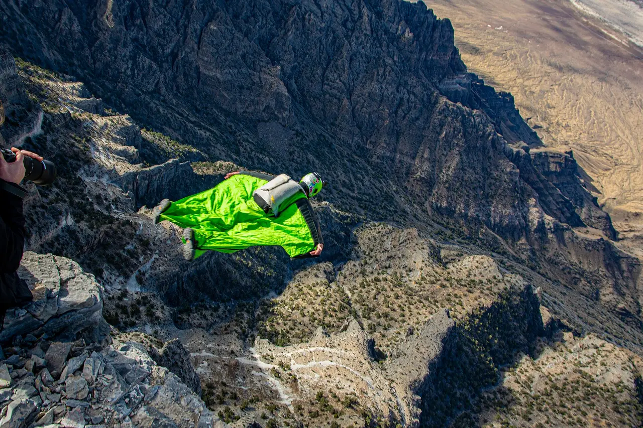 Flyer in a green wingsuit gliding above a rocky mountain face