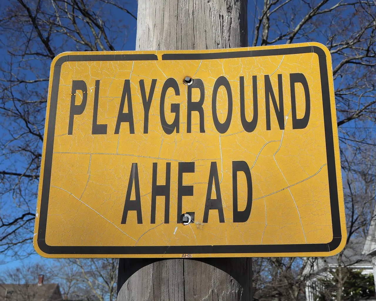Yellow road sign reading Playground Ahead on a wooden pole