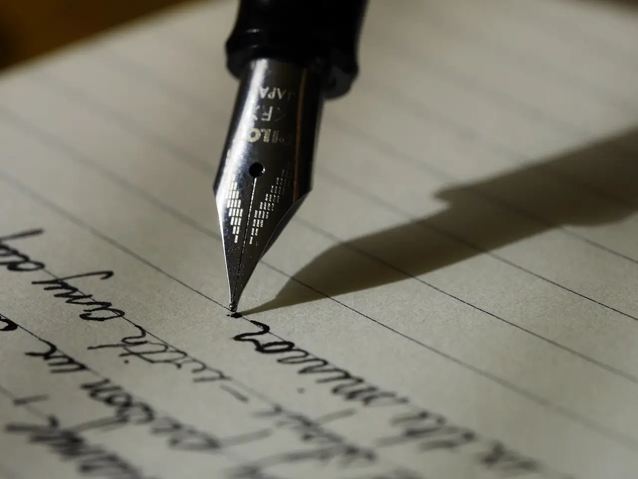 A fountain pen nib writing cursive on lined paper