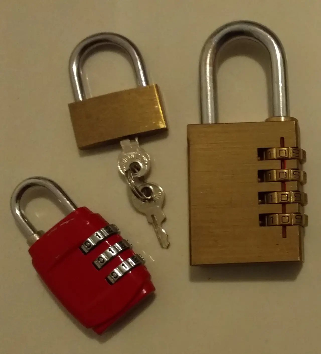 Brass and red padlocks with keys on a plain surface