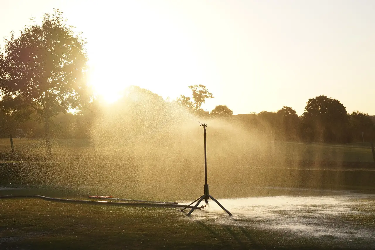 Sprinkler on a tripod spraying water over a lawn at sunset