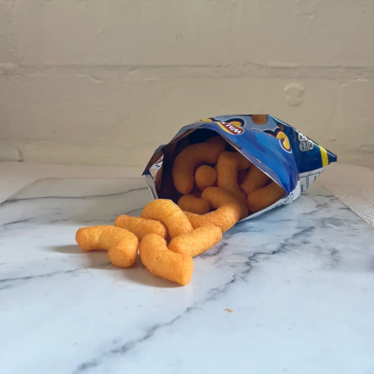 An open snack packet on a marble surface with orange cheese puffs spilling out