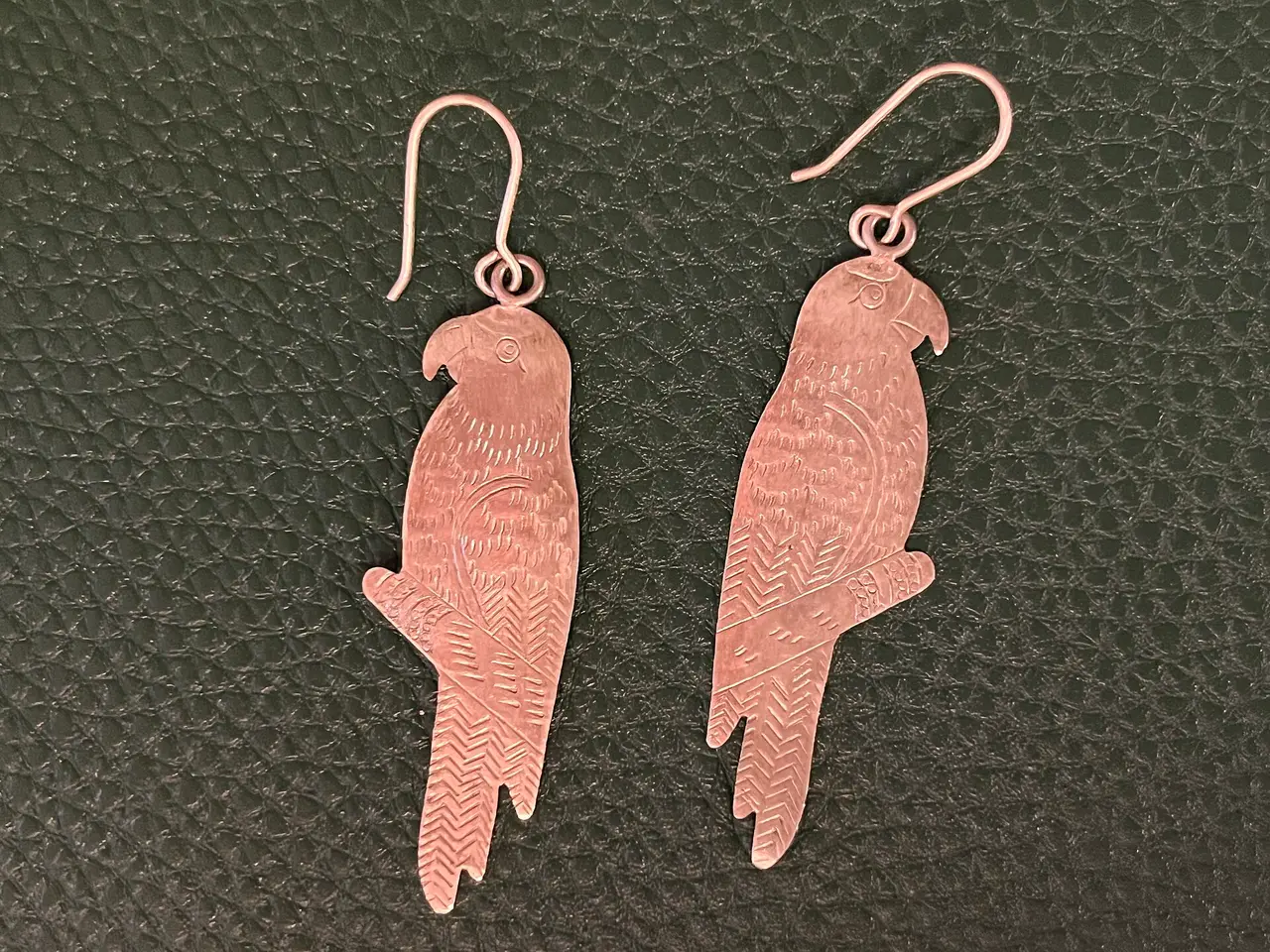 Two silver parrot-shaped earrings on green leather