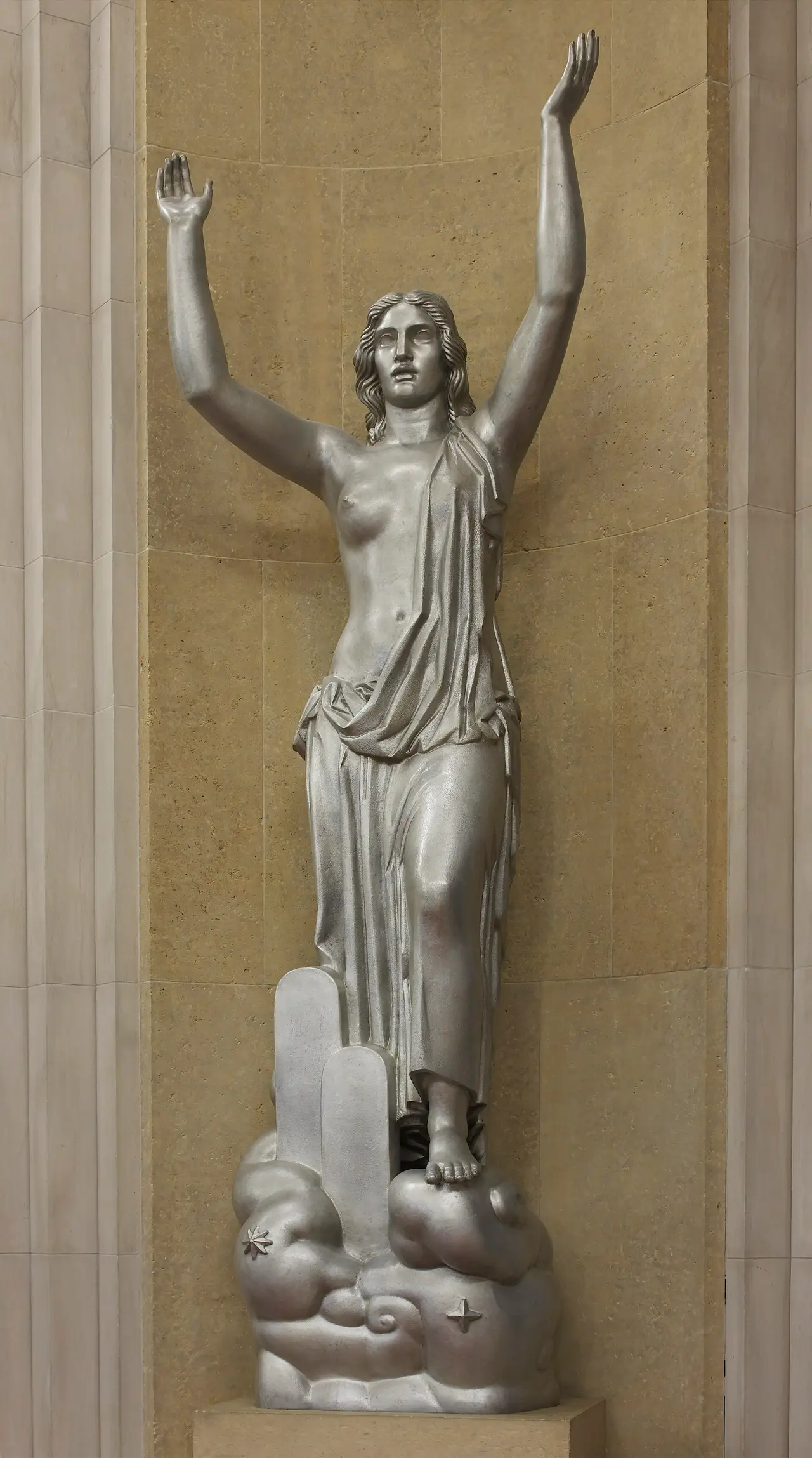 A pale statue of a woman with raised arms in a marble hall