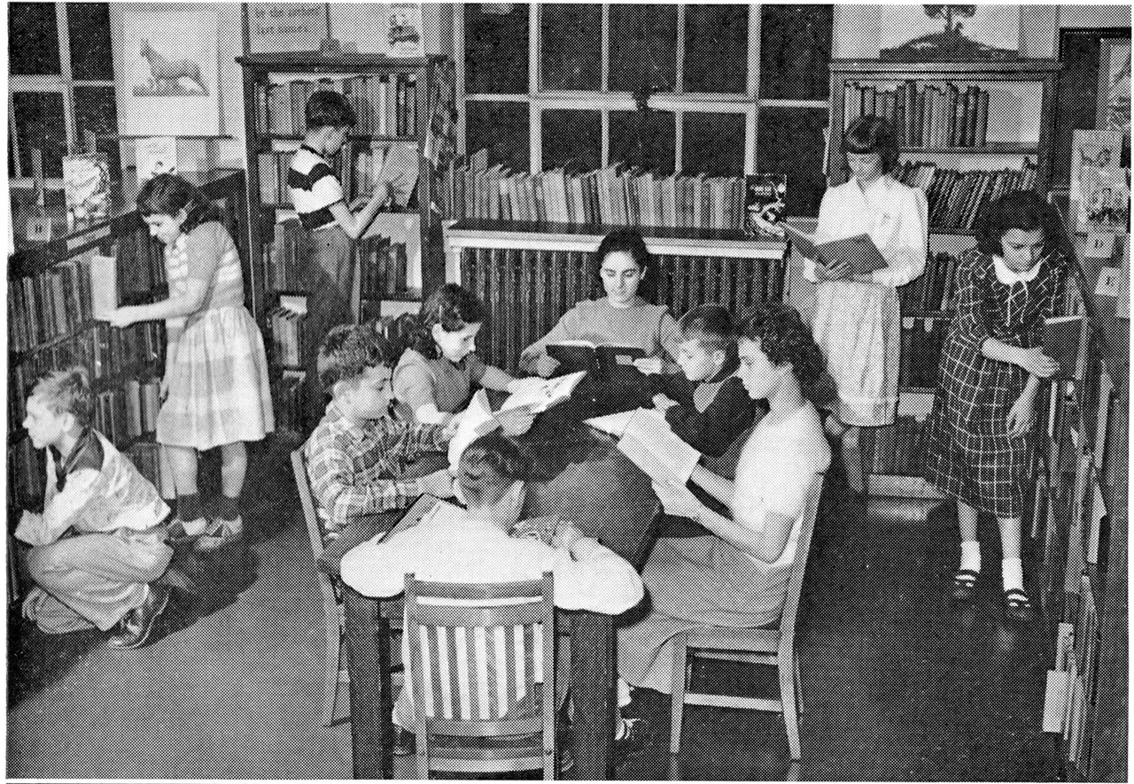 Children reading at tables and shelves in a 1945 library reading room