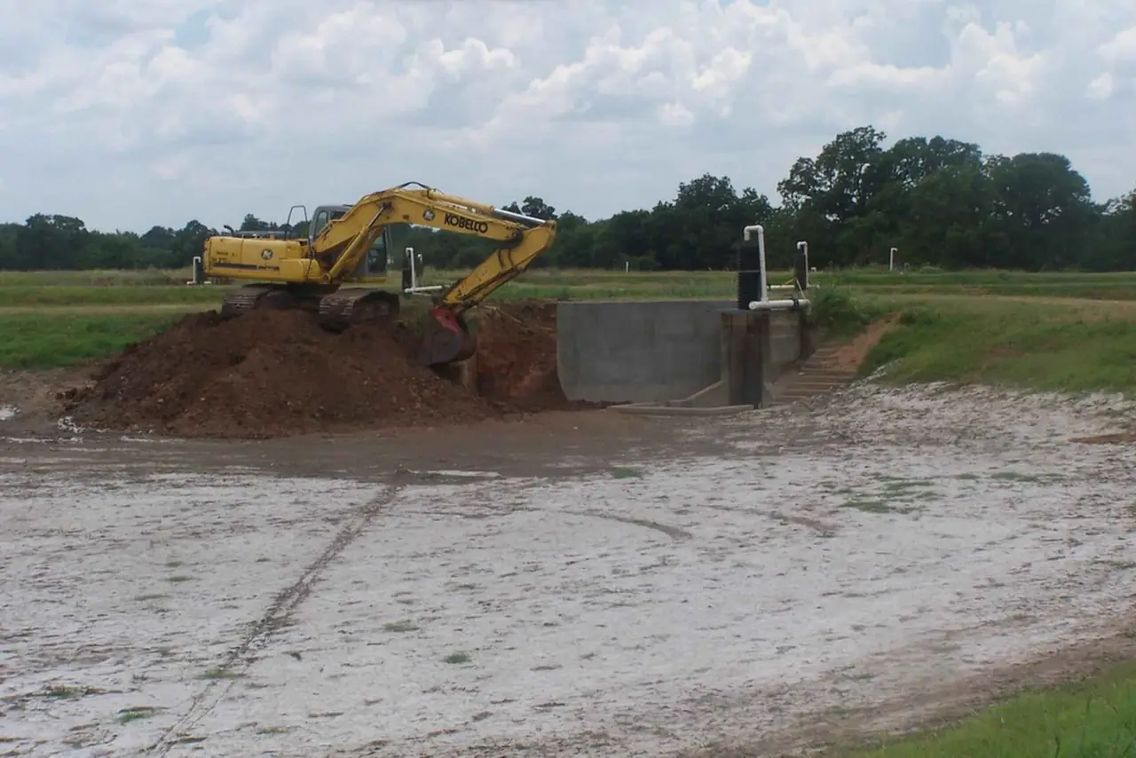 A yellow excavator working on a mound of earth in a field