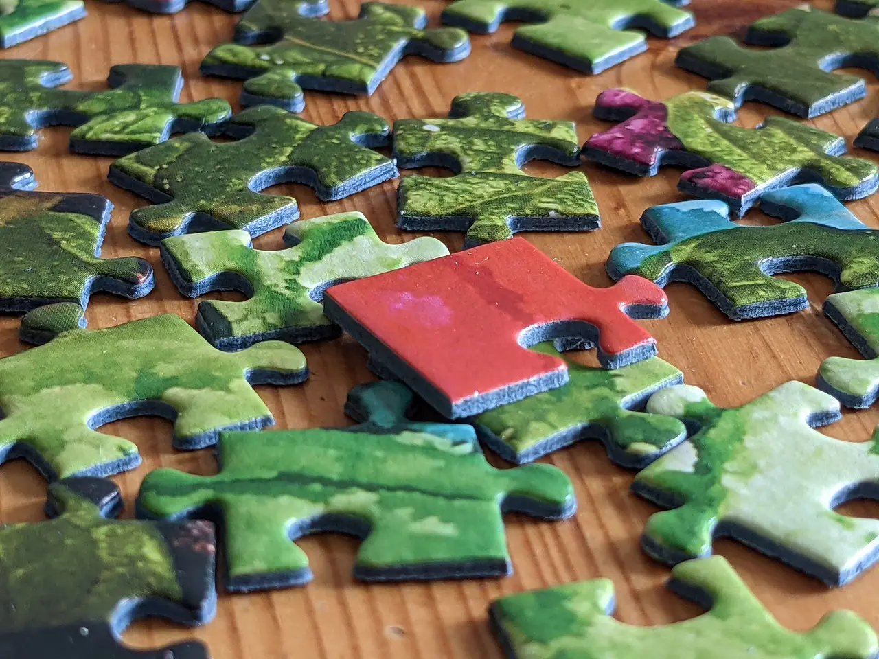 One red jigsaw piece resting on a heap of green pieces