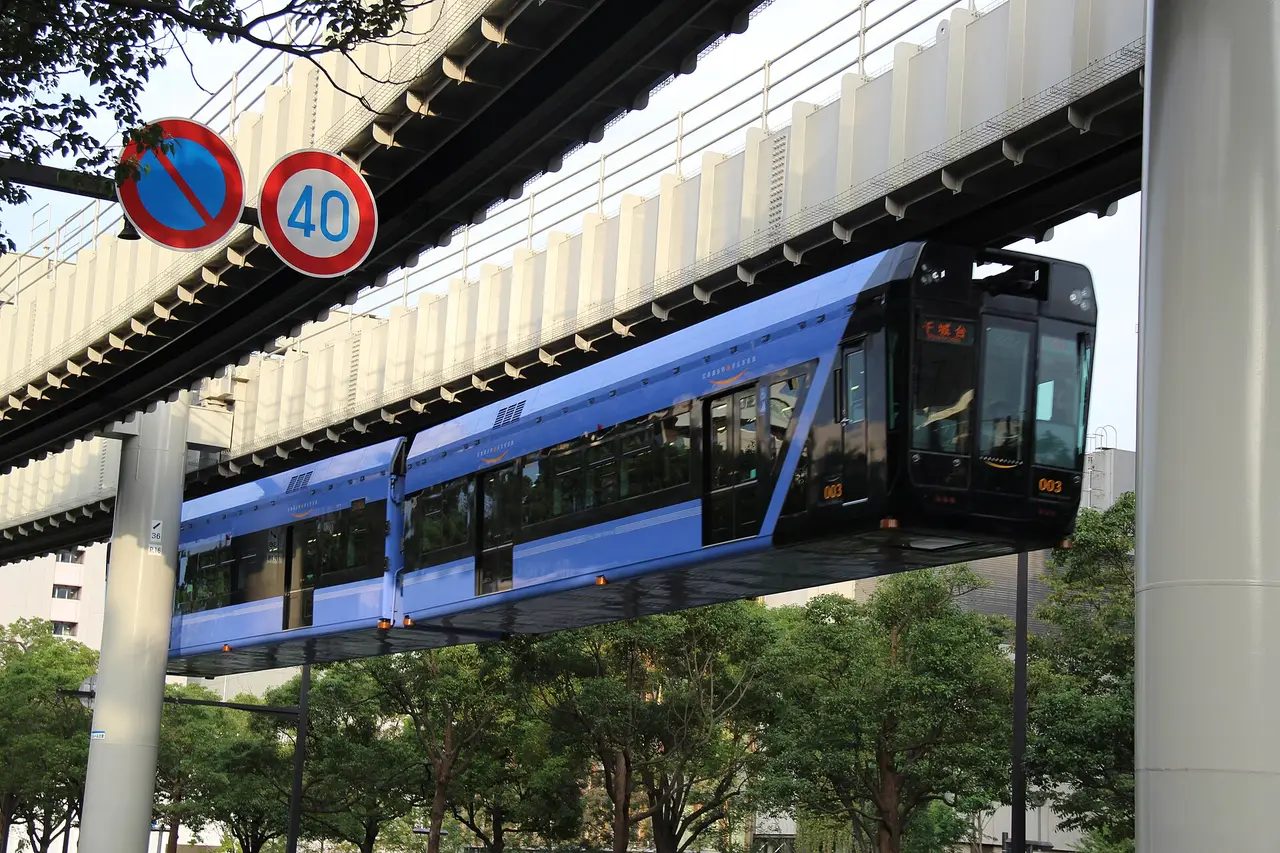 A blue suspended monorail train under an elevated track in Chiba