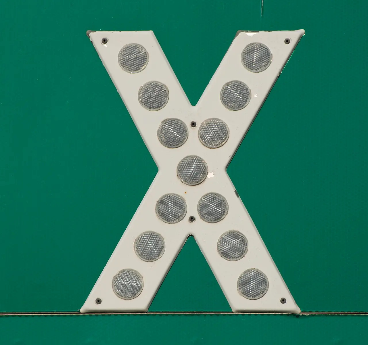 White letter X studded with round reflectors on a green sign