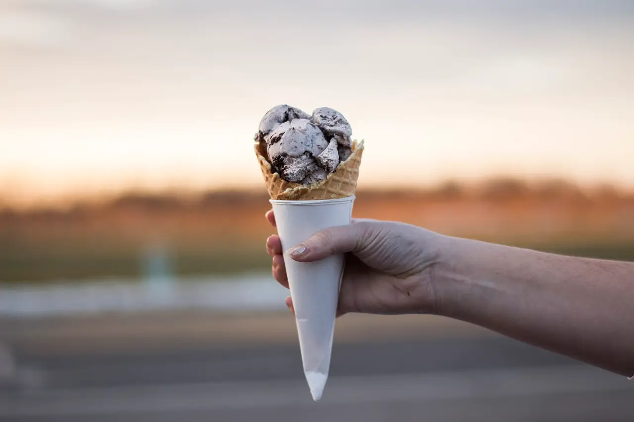 A hand holding a cone with two scoops of ice cream