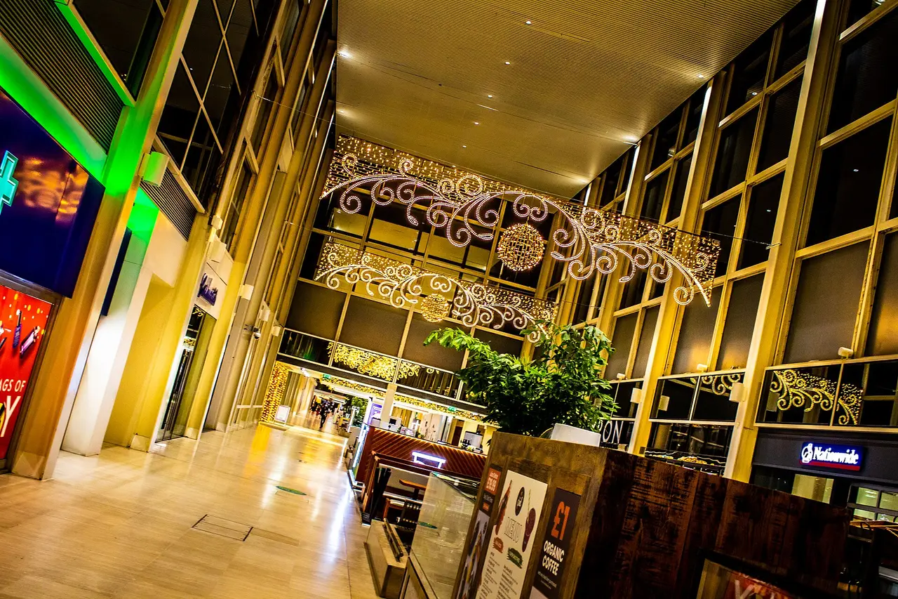 A glass-roofed shopping mall walkway with Christmas lights overhead