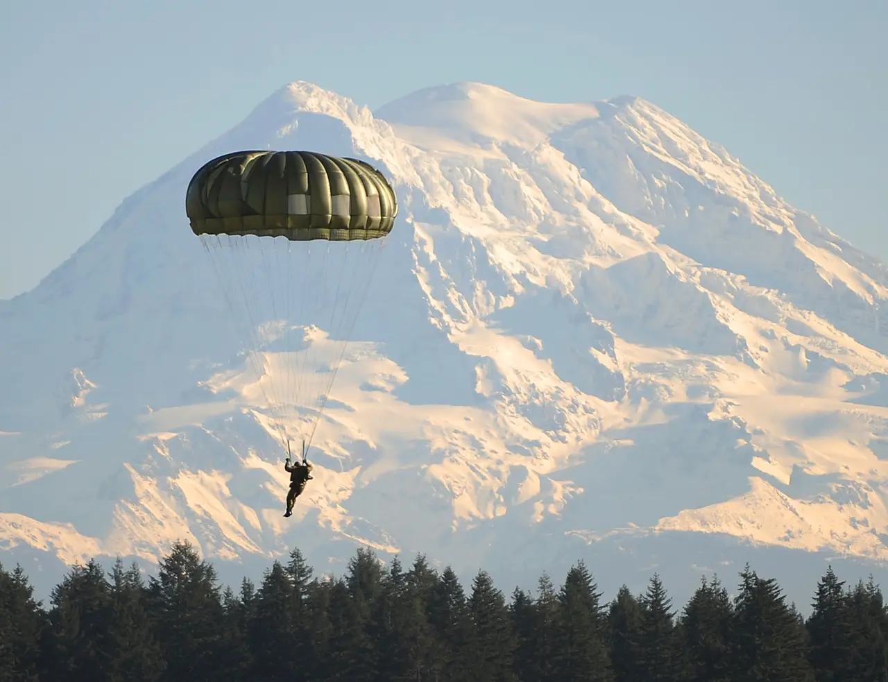 A parachutist drifting down in front of a snowy mountain