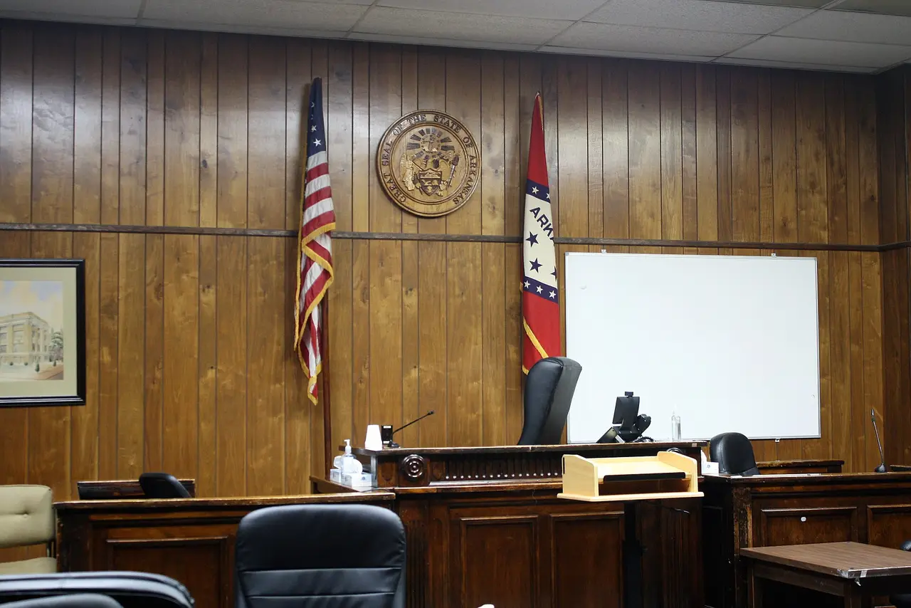 A wood-panelled courtroom with a raised judge's bench and two flags