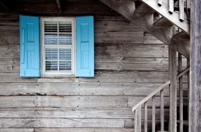 blue shutters at window and stairs on grey wooden facade