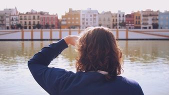 back view of person looking at colorful buildings through river, spain, seville